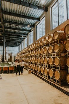 Spacious distillery interior featuring stacked wooden barrels and a group of people exploring.